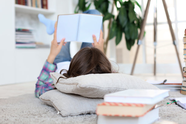 年轻女学生在家学习，准备大学考试，在地板上靠着舒适的室内装饰，周围堆满了书图片下载