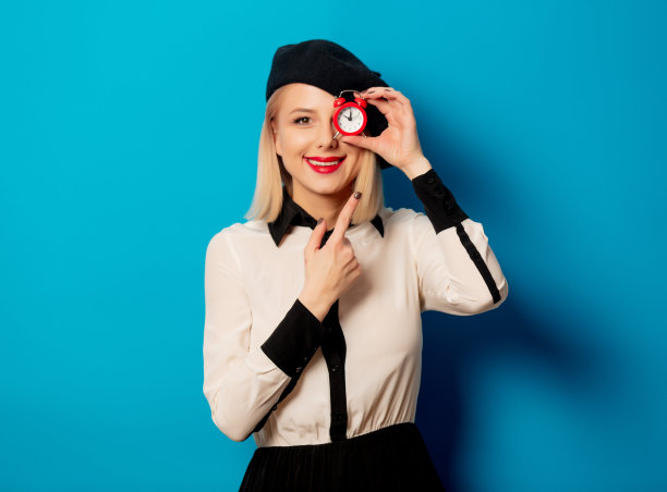 美丽的法国女人在贝雷帽持有红色闹钟在蓝色的背景图片下载