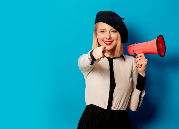 美丽的法国女人在贝雷帽手持扬声器在蓝色背景图片下载