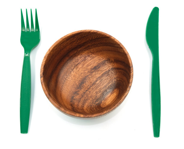 餐具对比刀叉绿色塑料碗附近的木纹。在白色背景上隔离图片下载