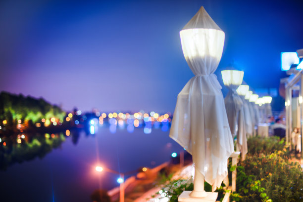 夜晚城市灯光与美丽的河流和树木。浪漫的氛围。晚上的天空是蓝色的。图片下载