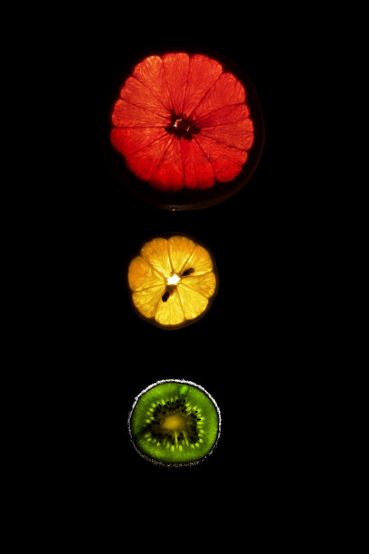 黑色背景下的柚子、猕猴桃和柠檬片在黑暗中闪闪发光图片下载