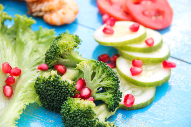 新鲜的蔬菜和水果沙拉在蓝色的复古桌子上。这张照片是一个古老的食物背景。花椰菜，石榴，橙子，西红柿和卷心菜一起。这是健康饮食的一个完美例子。图片下载