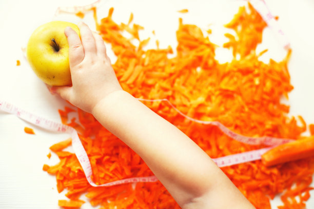 切碎的胡萝卜和苹果。孩子拿了一个苹果。水果和蔬菜是健康的饮食食物图片下载