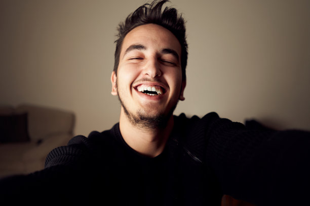 可爱的年轻男子看着相机和微笑在家庭工作室。真人带着笑脸独自自拍图片下载