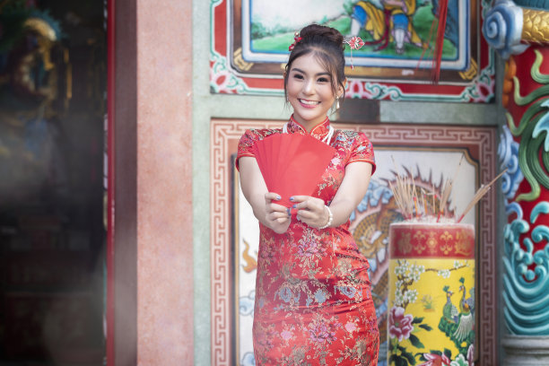 庆祝中国新年的概念:身着红色旗袍的中国妇女拿着红包在神祠。图片下载