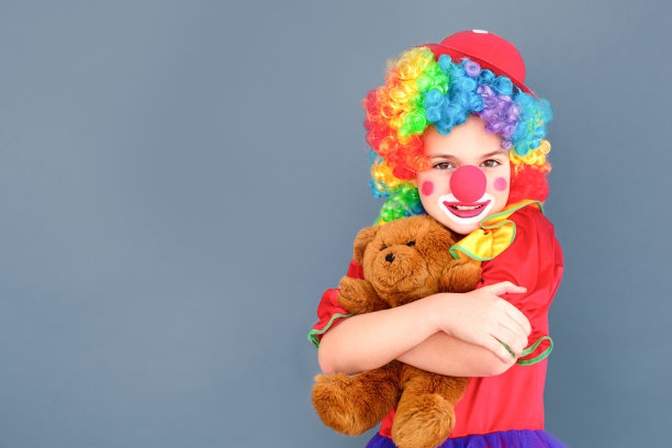 穿着小丑服的小女孩拥抱着玩具熊，露齿微笑图片下载
