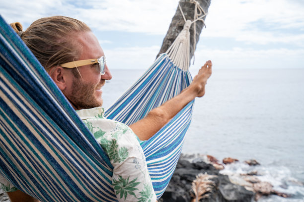 一名男子躺在挂在海滩棕榈树上的吊床上休息图片下载