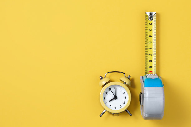 卷尺和闹钟隔离在黄色背景上。木匠和建造概念。图片下载