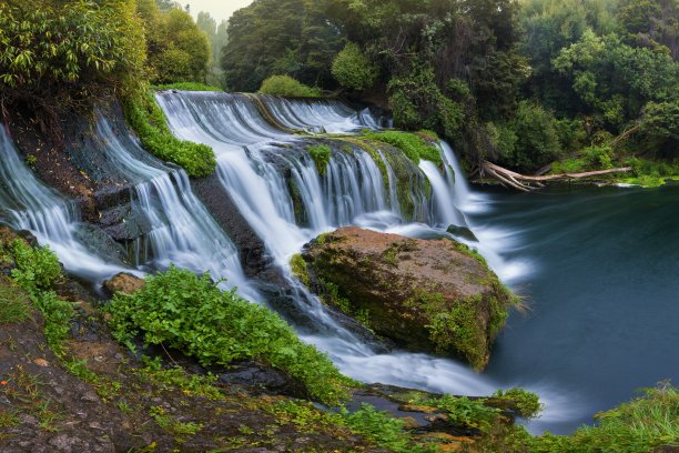 全景照片景观/瀑布隐藏在热带丛林周围的自然游泳池与清澈的水在背景绿色的森林树和山，新西兰图片下载