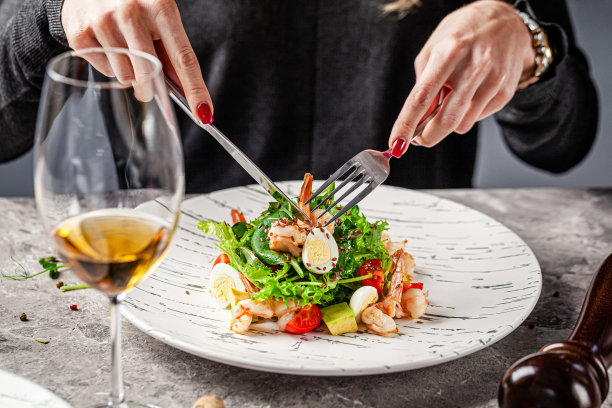 女孩在餐厅吃凯撒沙拉海鲜和虾。桌上有一杯白葡萄酒。饭店的现代服务。的背景图片。本空间图片下载