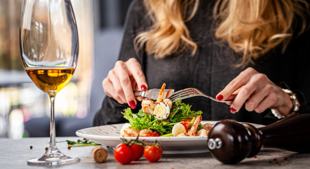 女孩在餐厅吃凯撒沙拉海鲜和虾。桌上有一杯白葡萄酒。饭店的现代服务。的背景图片。本空间图片下载