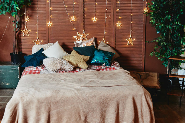 卧室内部有舒适的床，彩色的枕头和木墙上的星星花环，复制空间。舒适的家。新年快乐。圣诞装饰品图片下载