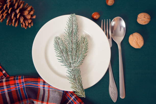 空的白色盘子，松枝，餐具和圣诞装饰在绿色的背景。前视图。本空间图片下载