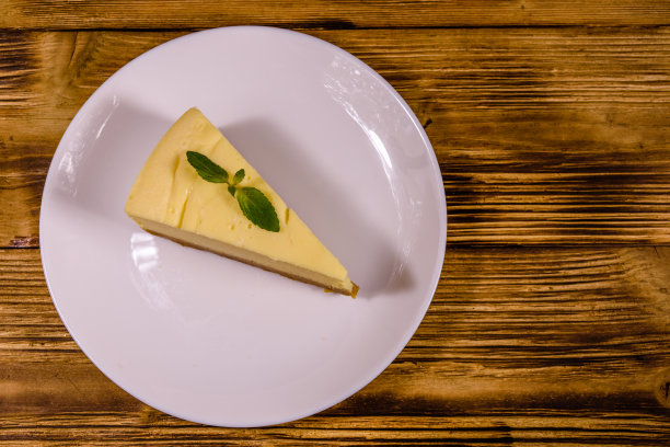 白色盘子，纽约芝士蛋糕和薄荷叶放在木桌上。俯视图图片下载