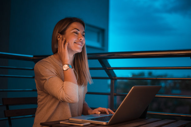 迷人的年轻女子打电话和使用笔记本电脑在晚上。图片下载