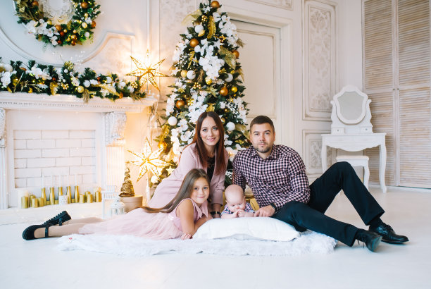 爸爸、妈妈和可爱的小朋友们躺在圣诞树旁的地板上。图片下载