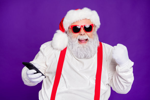 噢,是的。灰色头发的圣诞老人父亲拿着电话的照片现代技术用户赢得最佳送货服务奖穿太阳眼镜服装孤立的紫色背景图片下载