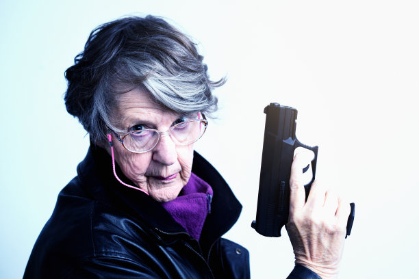 年长的女人扮演詹姆斯·邦德，高举手枪图片下载