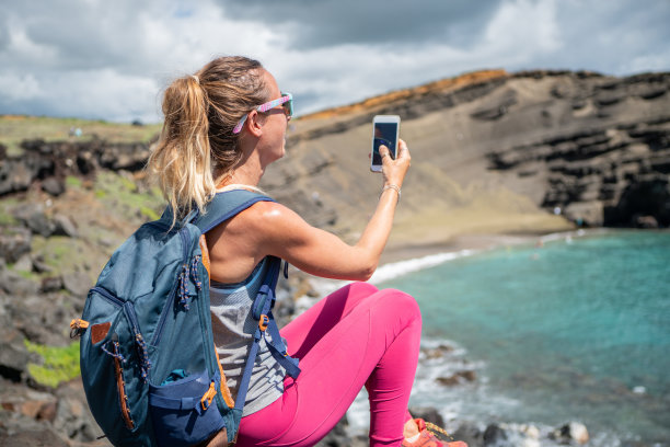 在夏威夷绿色沙滩上休息和使用手机的徒步妇女图片下载