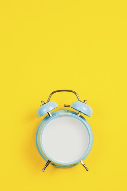 复古的蓝色空白闹钟在黄色的背景与马蹄莲作为装饰图片下载