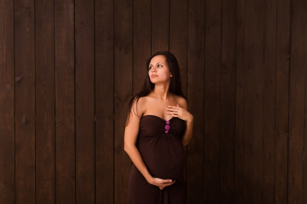 身着棕色衣服的孕妇双手搭在深棕色的腹部上。怀孕，母性，期望概念。美丽柔情的怀孕照片图片下载