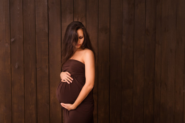 身着棕色衣服的孕妇双手搭在深棕色的腹部上。怀孕，母性，期望概念。美丽柔情的怀孕照片图片下载