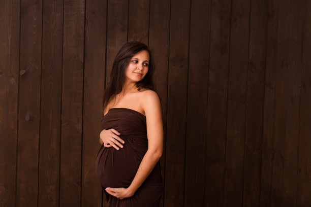 身着棕色衣服的孕妇双手搭在深棕色的腹部上。怀孕，母性，期望概念。美丽柔情的怀孕照片图片下载