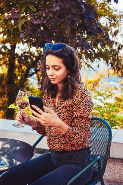 漂亮女人在户外用手机喝酒的照片。图片下载