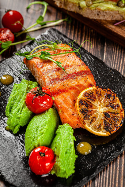 西班牙食品的概念。红鱼片。鲑鱼排配菠菜泥，配蔬菜，黑石板。的背景图片。副本的空间。图片下载