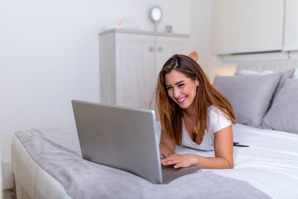 年轻漂亮的大学生在床上做家庭作业，年轻漂亮的女人准备学校考试在卧室用笔记本电脑。自由职业者在家工作的概念图片下载