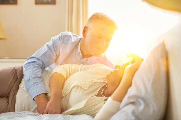 甜蜜的老年夫妇拥抱在床上与黄色镜头光晕图片下载