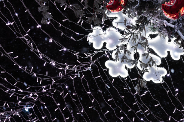 看这个由雪花和丝线组成的发光花环，红色的圣诞球映衬着夜空。图片下载