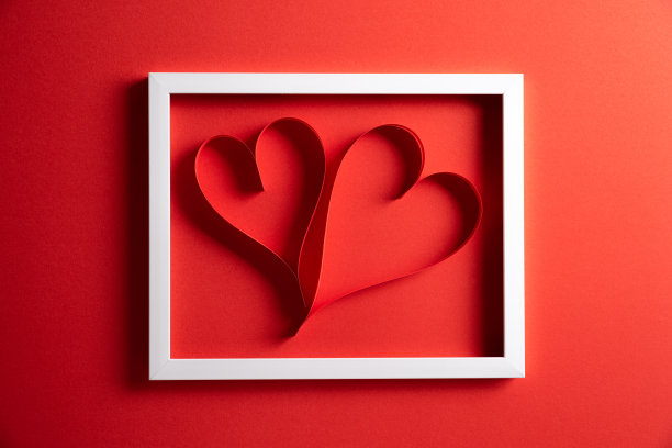 两颗红纸心在白色相框在红纸背景。爱情和情人节的概念。图片下载