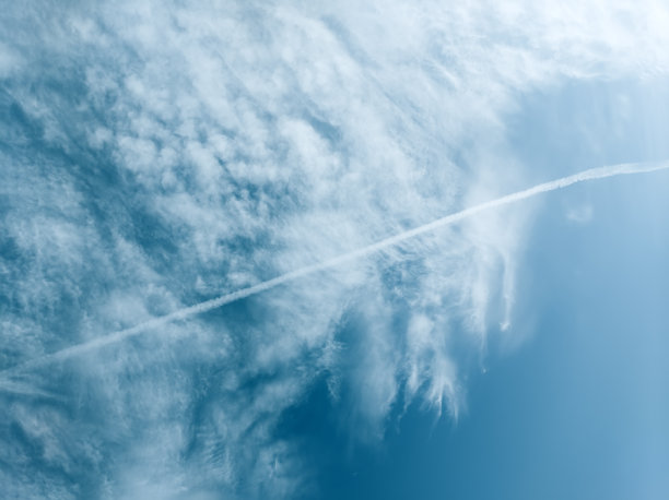 一架飞机在白云密布的蓝天上留下的逆温痕迹。图片下载
