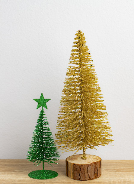 金色的圣诞树和绿色的小圣诞树放在棕色的桌子和白色的背景上图片下载