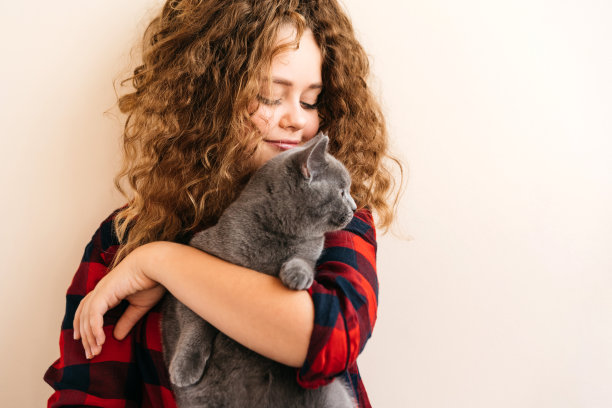 金发卷毛少女微笑着，手里拿着一只苏格兰品种的灰色小猫图片下载
