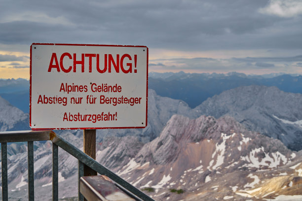 在阿尔卑斯山的山顶上，用德语写着:“小心。”高山地形，只适合登山运动员下山，有坠落危险”。图片下载