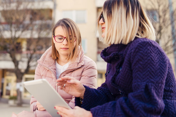 两个女性女性朋友在城市里使用电子平板电脑看图片或地图应用项目在冬天或秋天的一天谈论工作图片下载