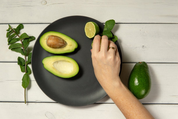 一个在白色木质背景上准备生鳄梨和酸橙的女人图片下载