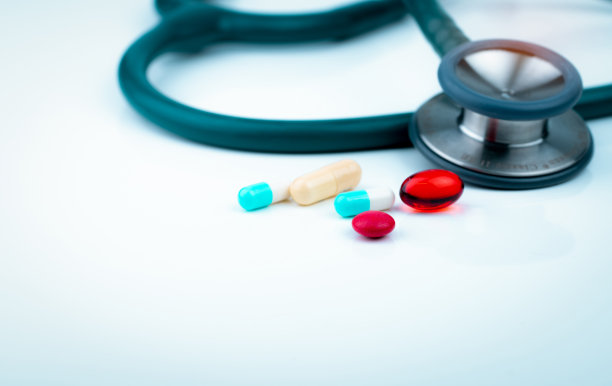 听诊器上有蓝白色胶囊、红色软凝胶胶囊丸剂、红色圆形丸剂，放在医生桌上或护士桌上。医疗保健和医学背景。心脏病医生诊断设备。图片下载