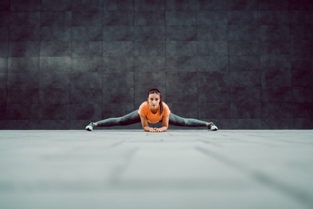 适合有吸引力的灵活的白人女运动员在户外运动服装做劈叉。背景是深色的墙壁。图片下载
