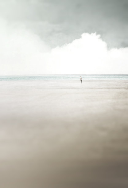极简的超现实景观，男人走在平静的海边的海滩上图片下载