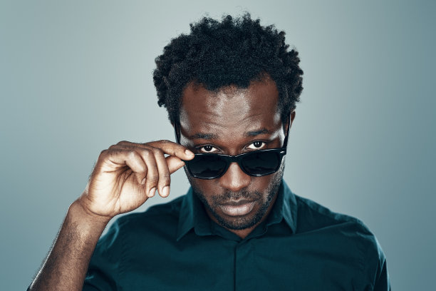 英俊的年轻非洲男子看着相机和调整眼镜，而站在灰色背景图片下载