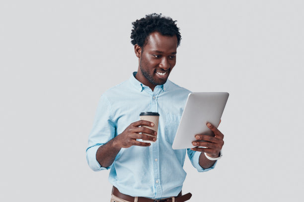 年轻英俊的非洲男子在灰色背景下微笑着使用数字平板电脑图片下载