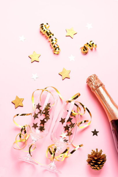 两个香槟杯，上面有粉色和金色的五彩纸屑和彩带，复制空间。圣诞或新年的节日平铺作文。粉彩背景上的创意圣诞贺卡图片下载