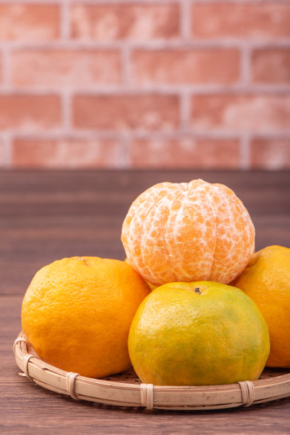 去皮的橘子放在竹筛篮上，深色木桌以红砖墙为背景，中国农历新年水果的设计理念，拉近了距离。图片下载