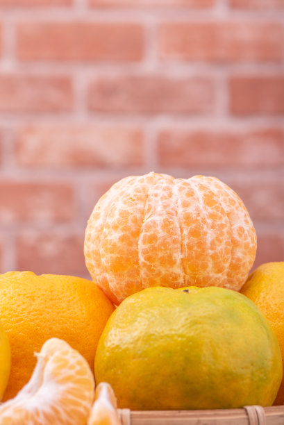 去皮的橘子放在竹筛篮上，深色木桌以红砖墙为背景，中国农历新年水果的设计理念，拉近了距离。图片下载