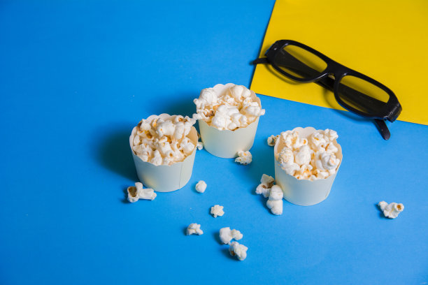 3个迷你小爆米花盒的特写镜头，装满新鲜热爆米花的杯子电影院3d眼镜黑色蓝色和黄色背景图片下载