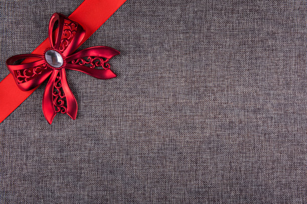 红色金属蝴蝶结和灰色粗麻布上的红色缎带图片下载